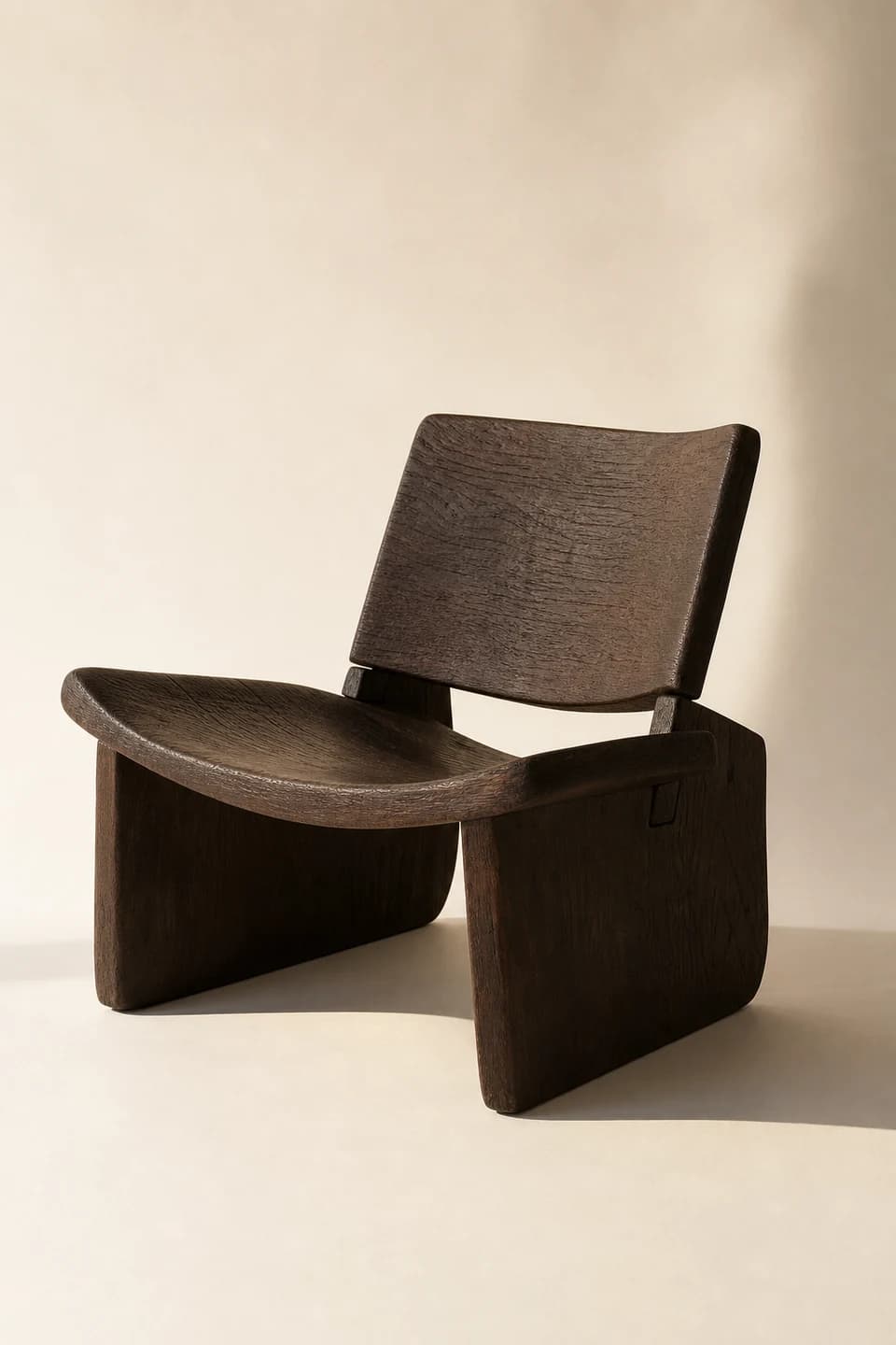 Low sculptural chair carved from dark smoked oak